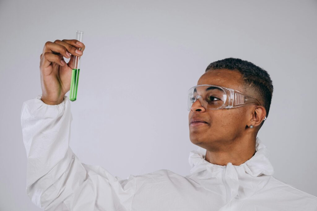 Young male scientist in protective gear examining a test tube in a laboratory setting.
